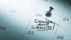Ημερολόγιο με πινέζα και σημείωση “Design Your Website” – έννοια προγραμματισμού επανασχεδιασμού ιστοσελίδας.